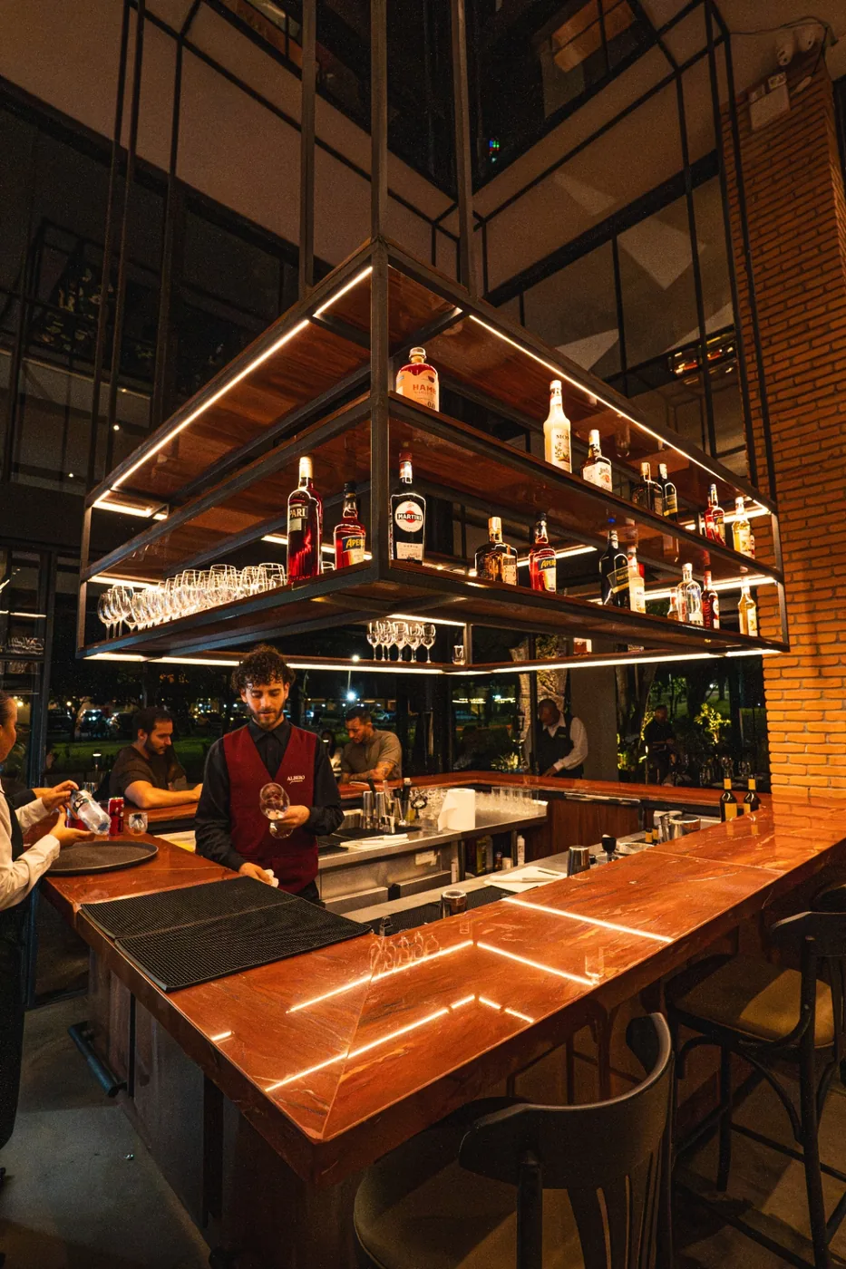 Bar em mármore vermelho da Albero com prateleiras retroiluminadas de destilados.