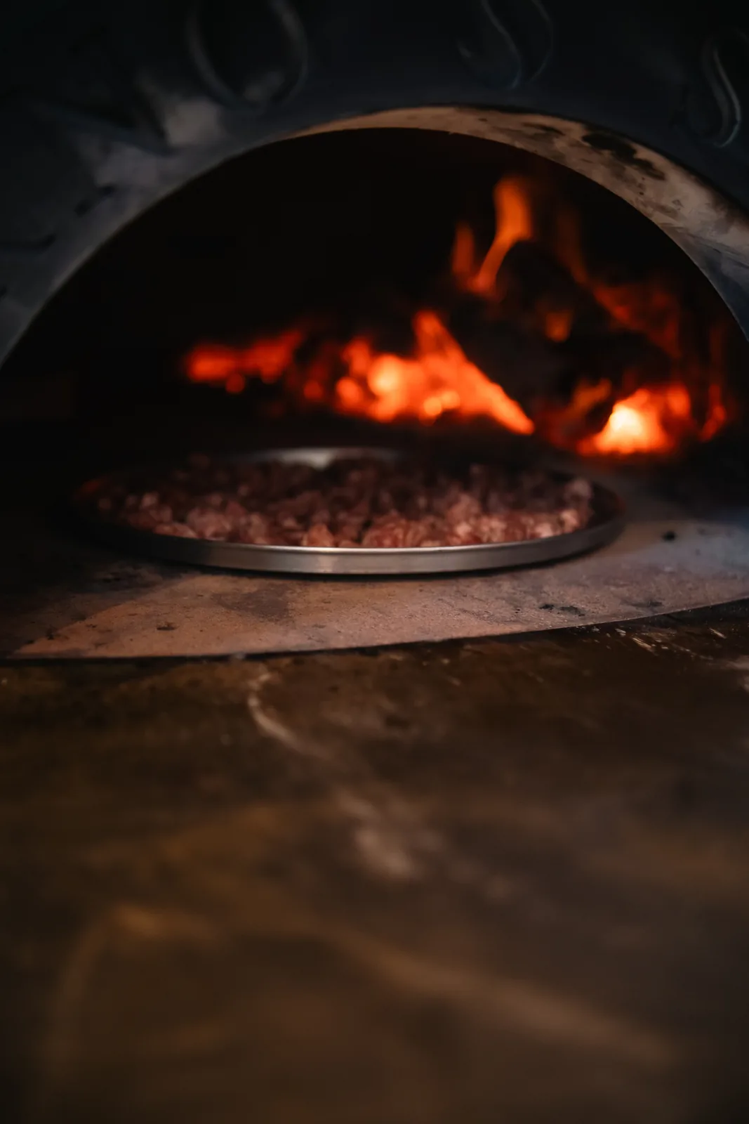 Pizza entrando no forno à lenha da Albero, com brasas incandescentes ao fundo.