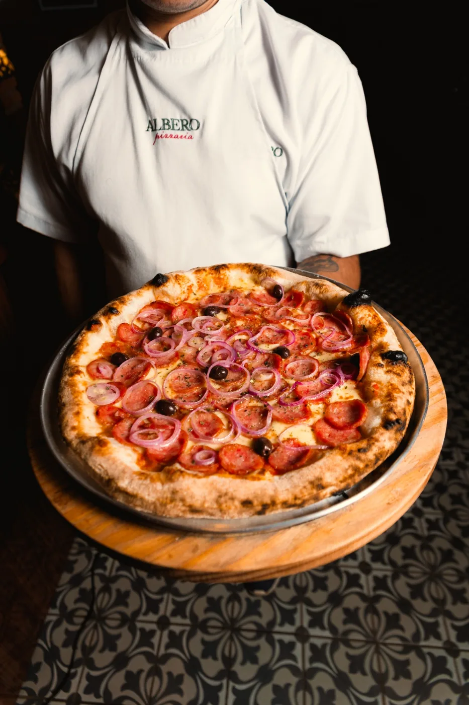 Pizza servida em tábua de madeira, com bordas de forno à lenha.