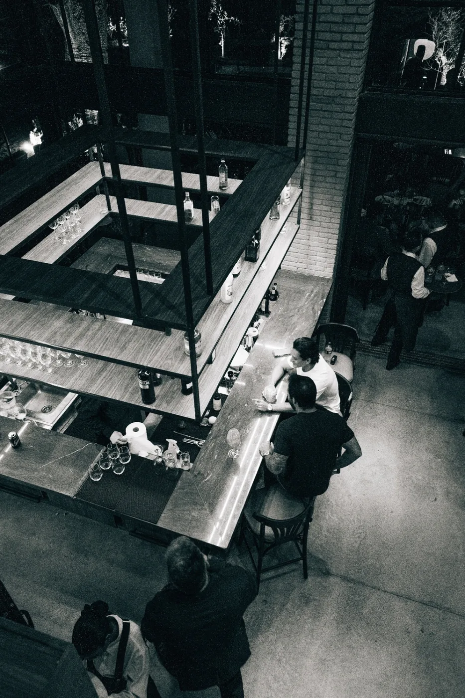 Vista superior do bar da Albero em preto e branco, com dois clientes ao balcão.